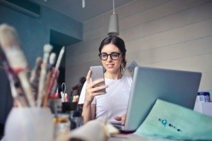 A girl using mobile phone in front of laptop. Smith Publicity book publicists uses media databases for book marketing, publicity and media PR.