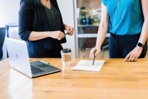 A Laptop on table beside two standing women having discussion. Smith Publicity social media book marketing and author pr services.