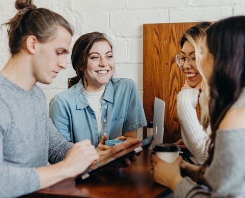 Young authors sitting around a table discussing how to use a vlog to promote books.